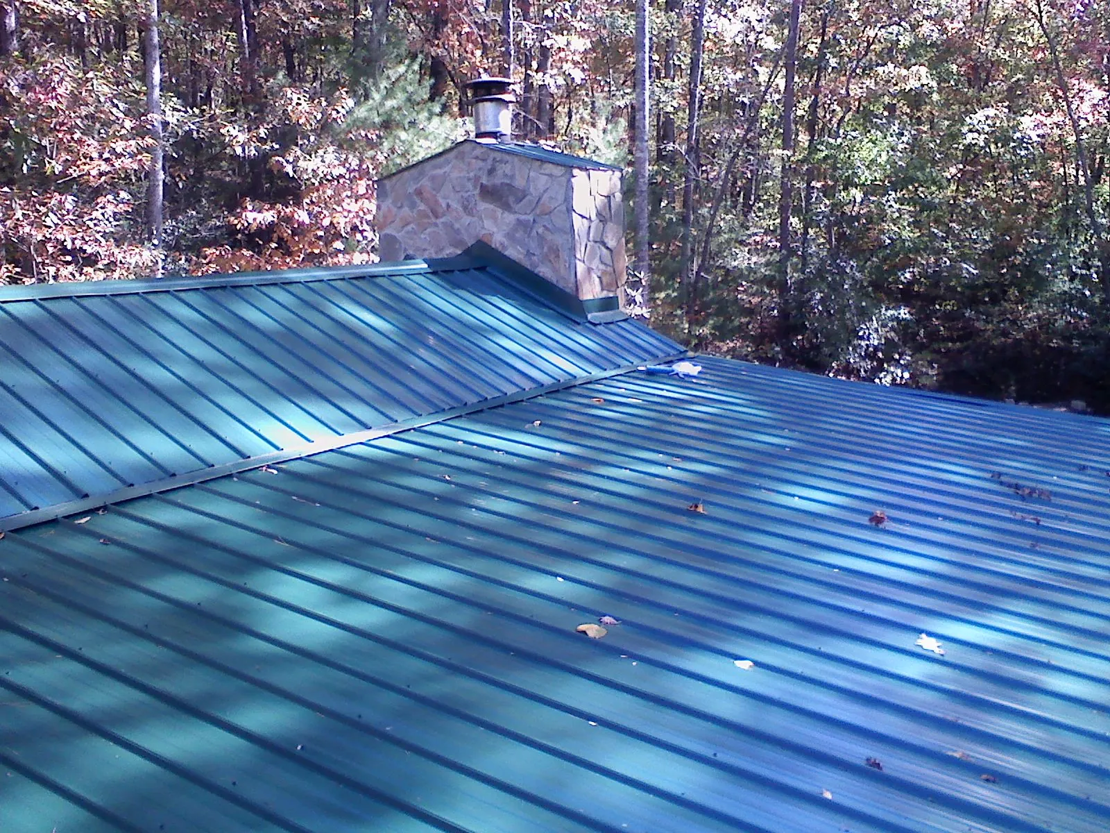 New green metal roof and stone chimney surrounded by autumn woods in Brooksville
