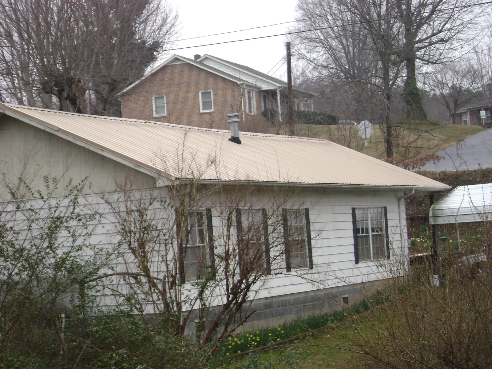 Tan metal roof on a white sided house set into a hillside — Commercial Roofing by Roofing Brothers in Brooksville